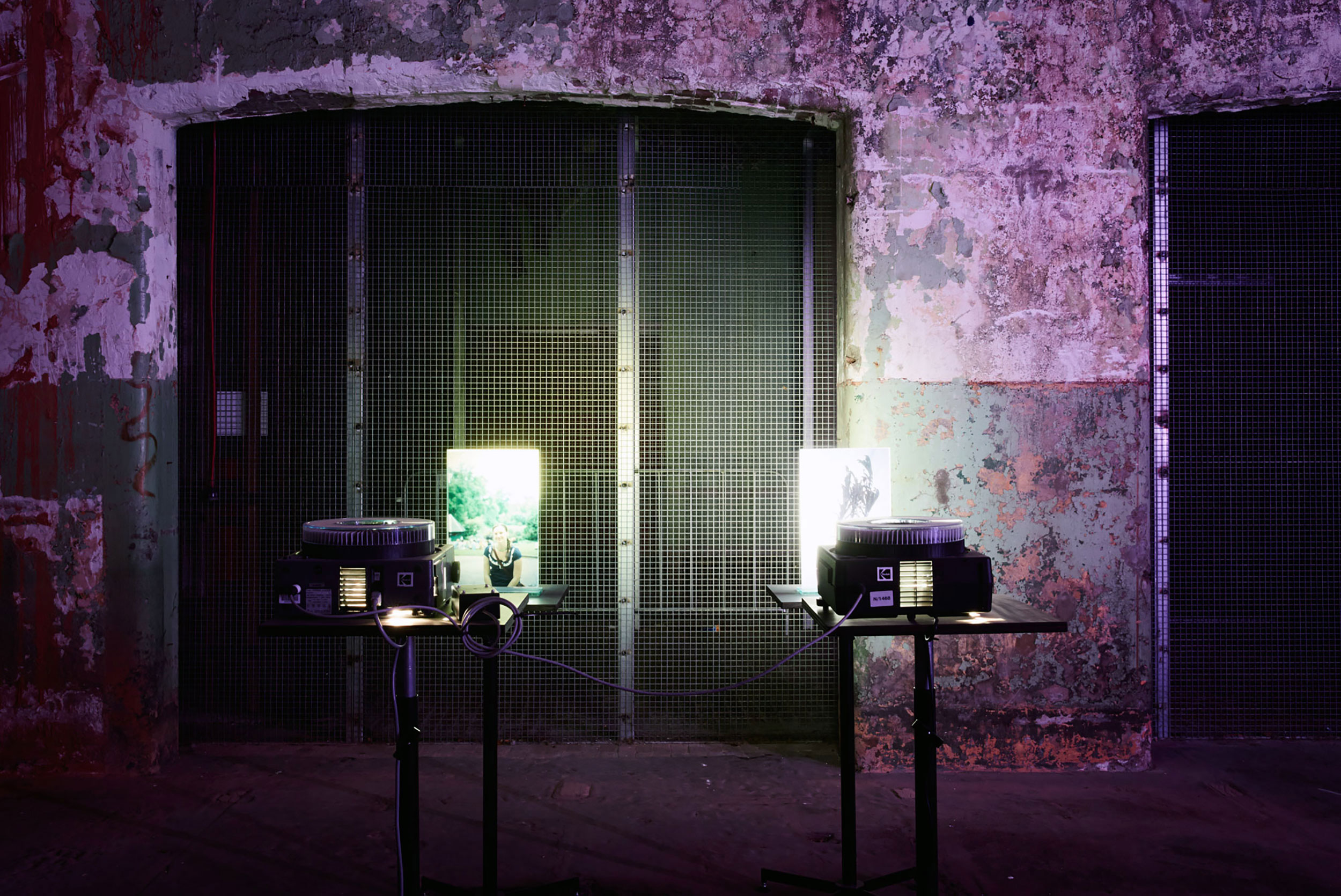 Pair of slide projectors with illuminated portraits against industrial mesh