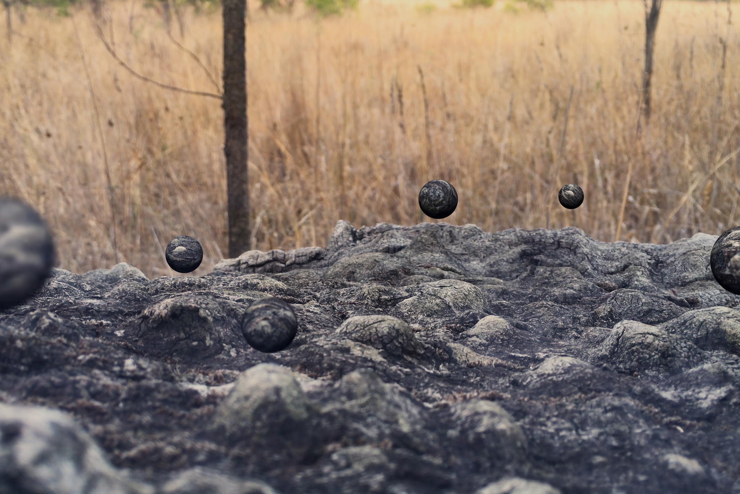 Still from Collider showing small dark spherical forms floating above textured rock