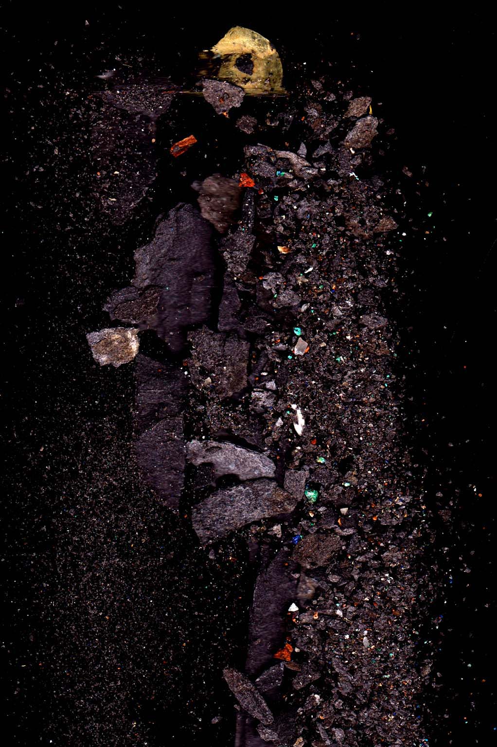 Vertical abstract image of dark mineral fragments and small coloured shards