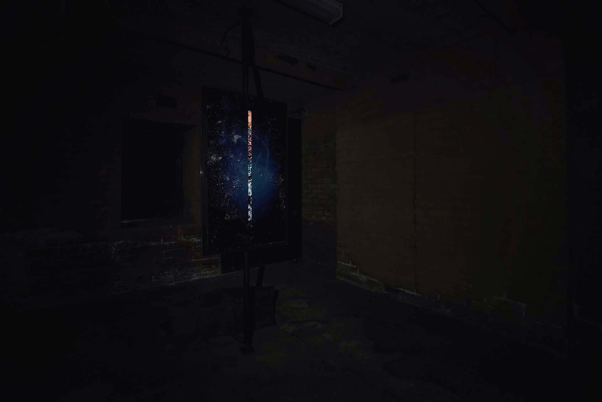 Dark installation view of a vertical artwork with a luminous central line