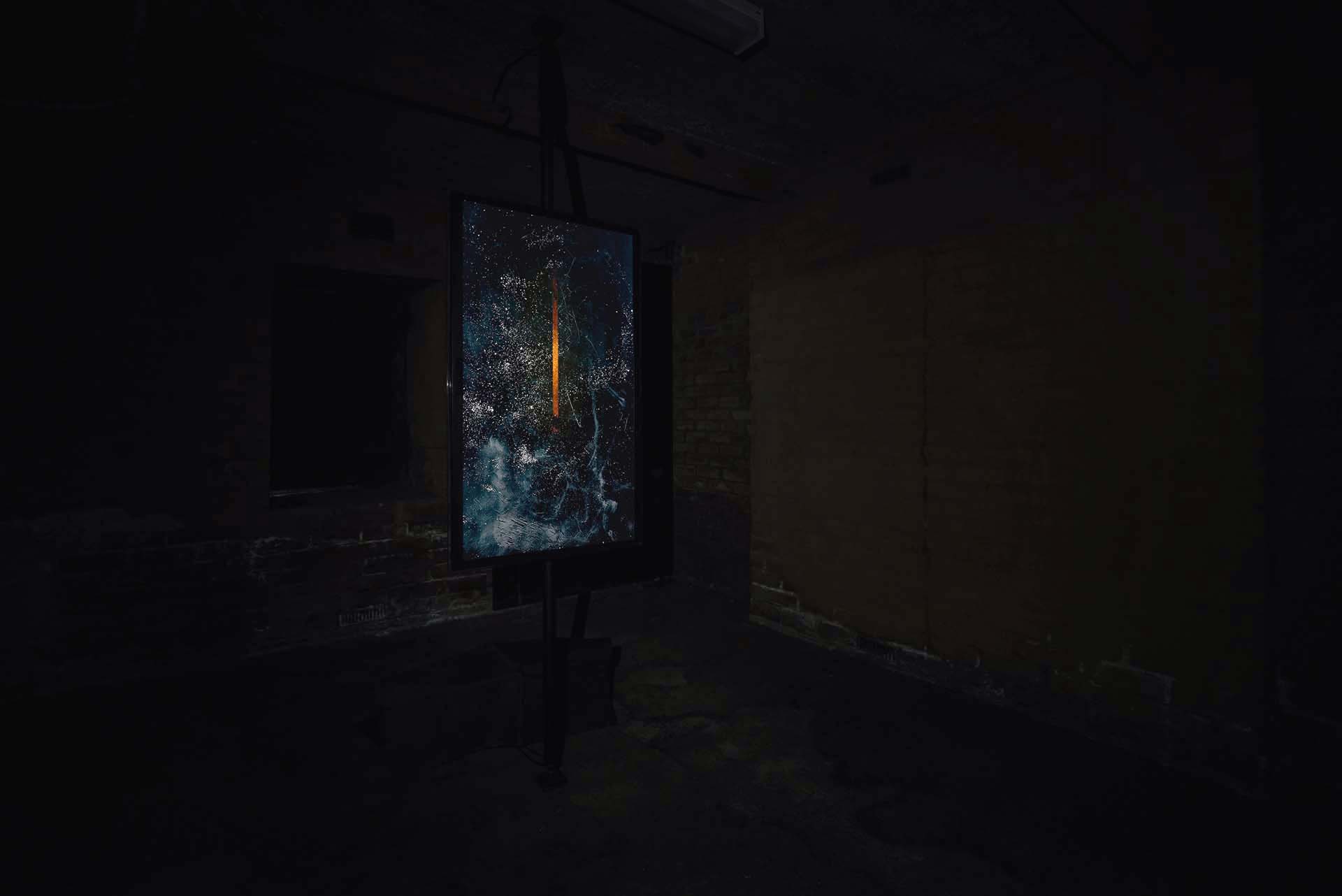 Dark installation view of a blue and orange vertical artwork