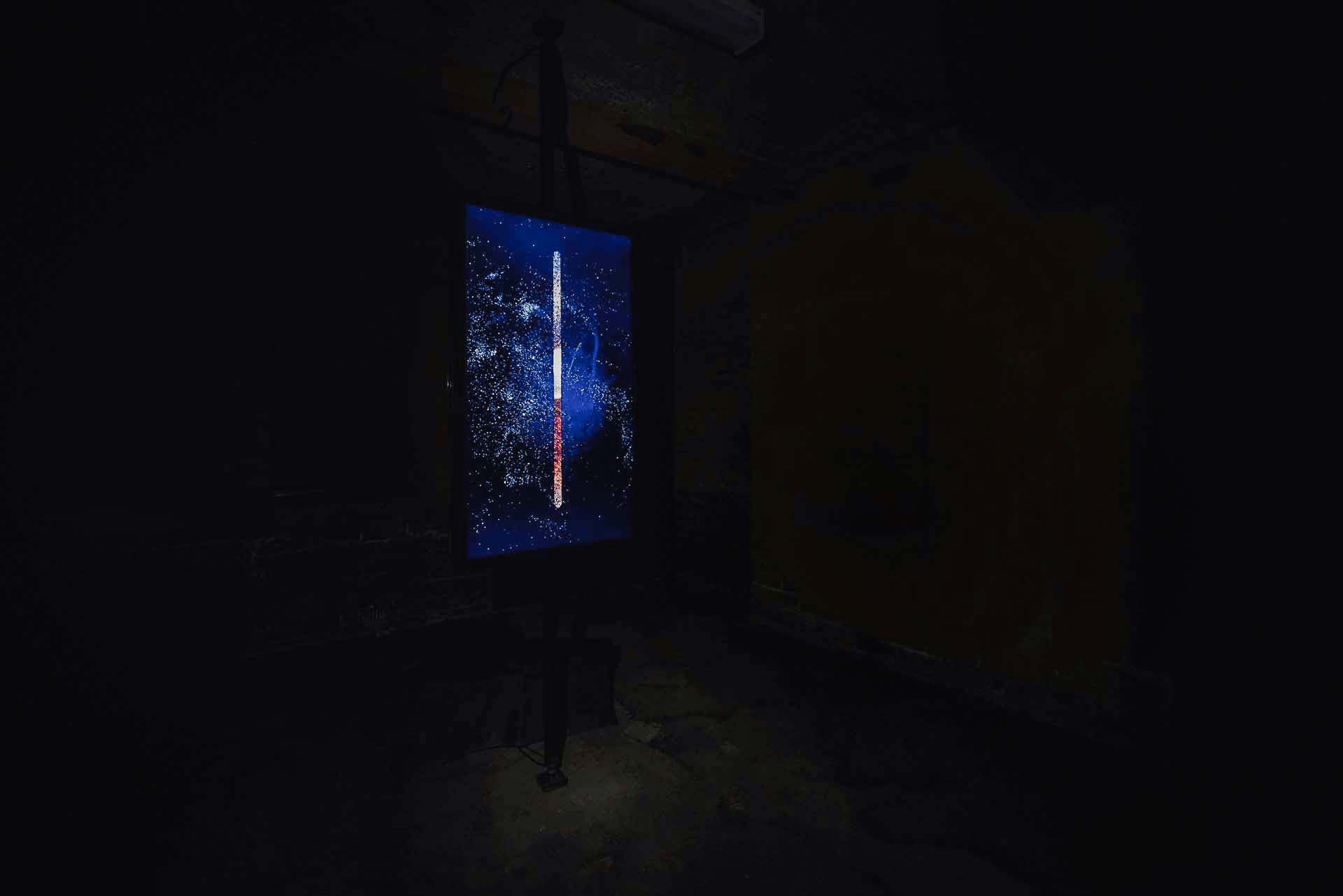 Dark installation view with a glowing blue vertical screen in Town Hall Underground