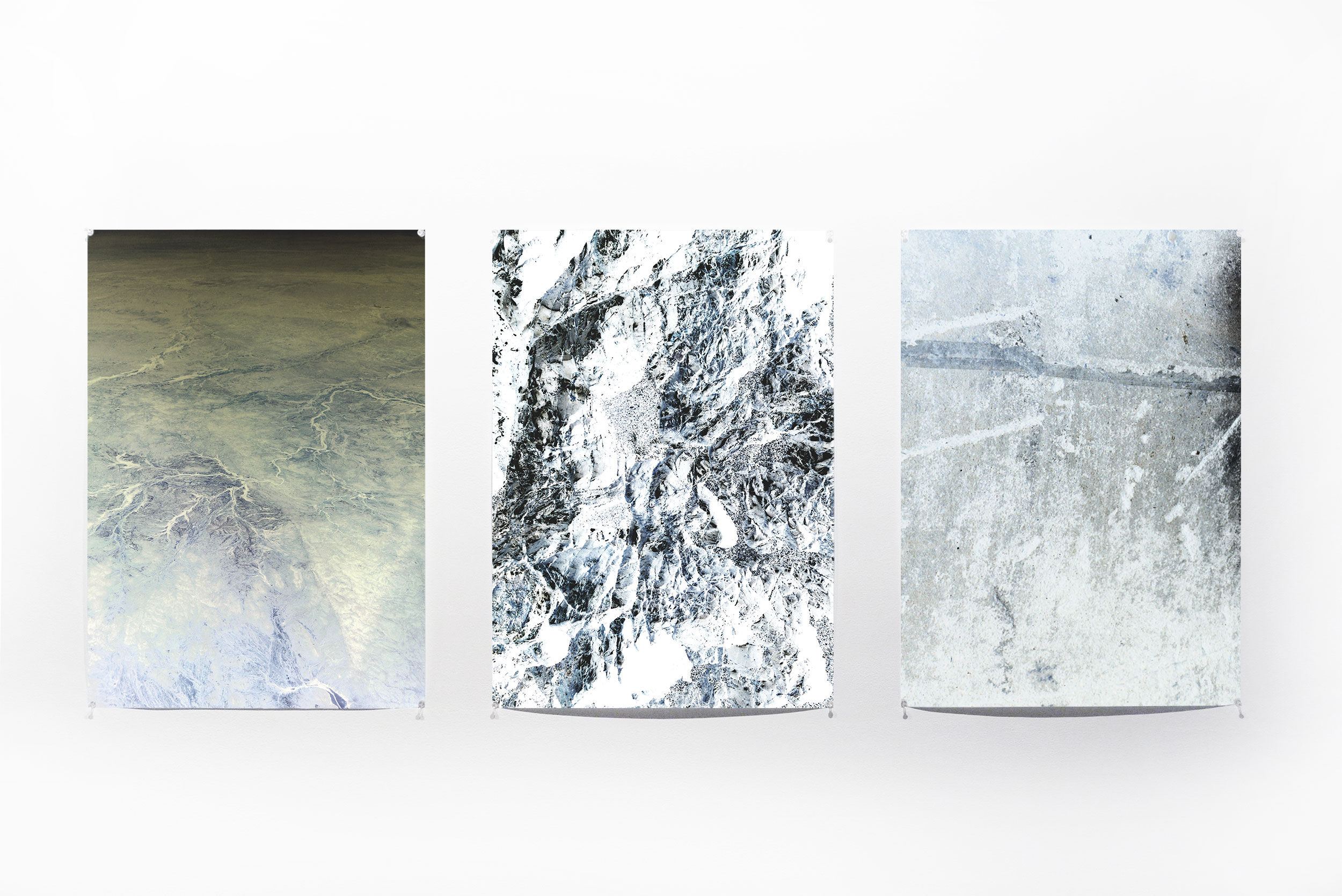 Three pale photographic works installed side by side on a white wall