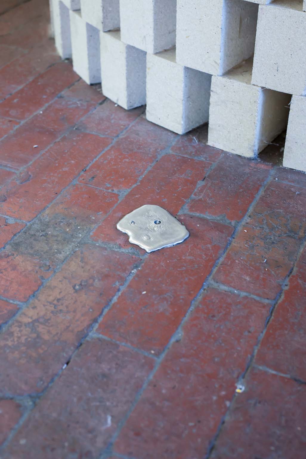 Small silver pewter ingot embedded in a red brick gallery floor beside a white brick structure