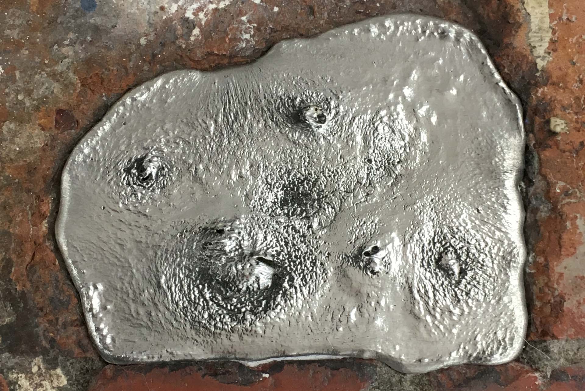 Close view of a silver pewter ingot set into a worn brick floor