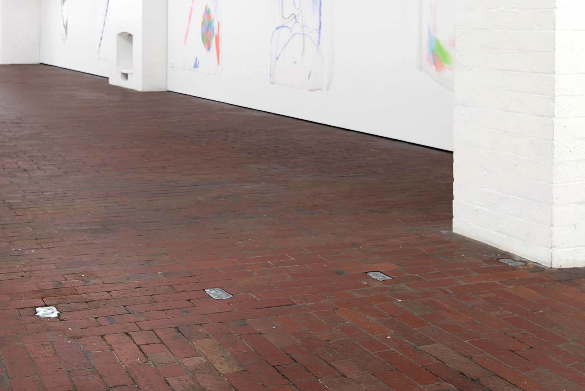 Several silver pewter ingots distributed across the brick floor of a white gallery