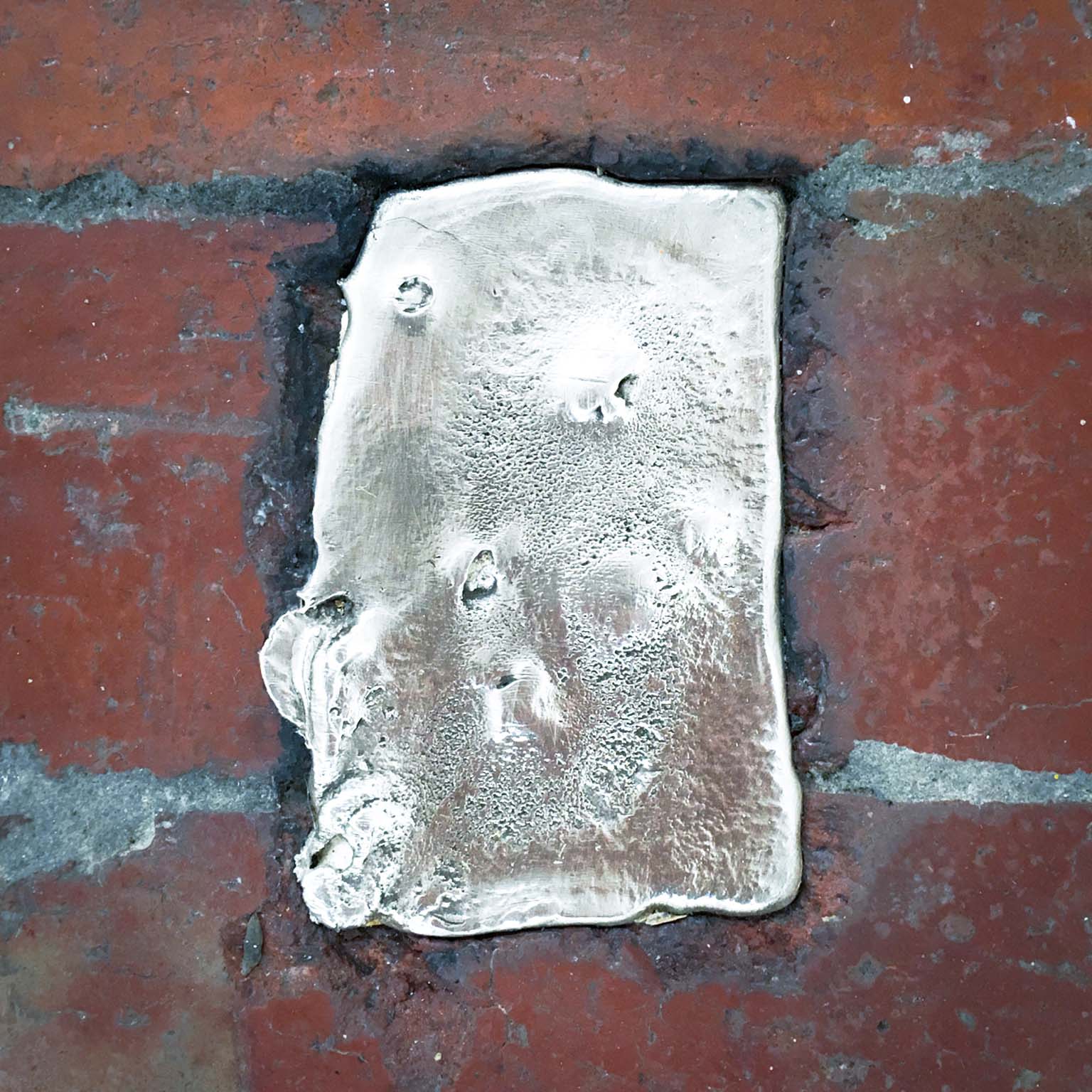 Rectangular silver pewter ingot fitted between worn red bricks