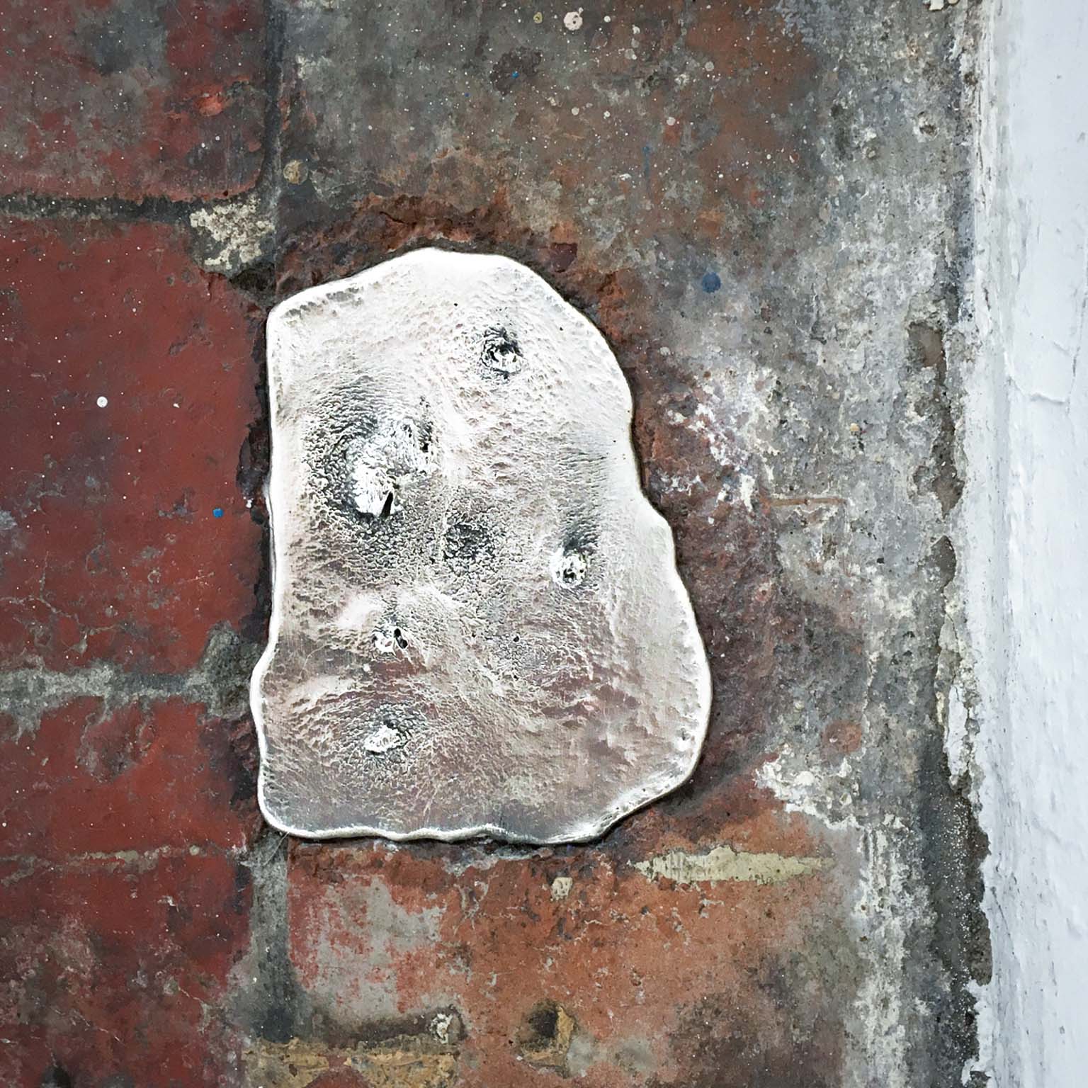 Irregular silver pewter ingot embedded at the edge of a brick floor