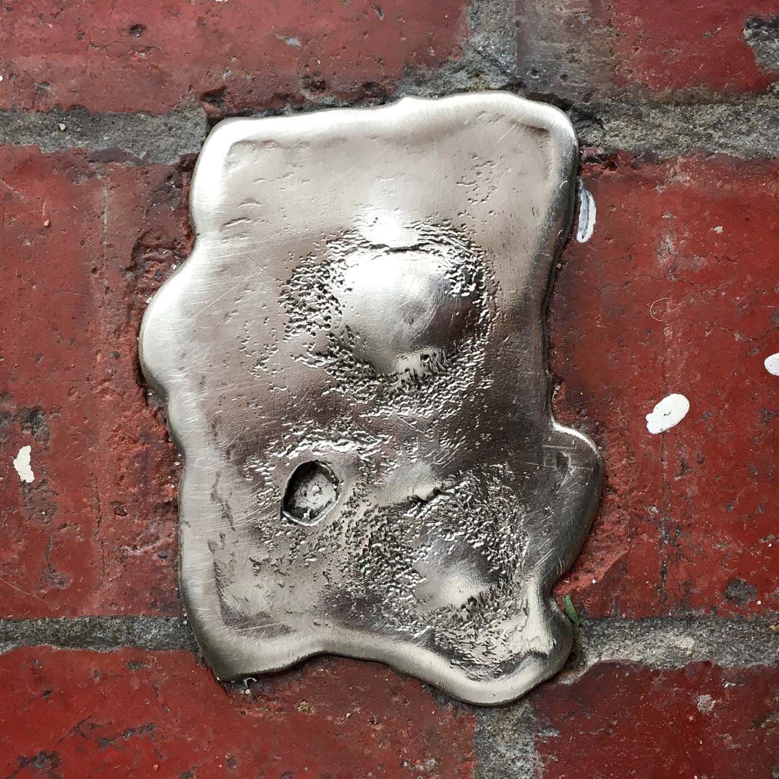 Polished silver pewter ingot with an irregular outline set into red brick